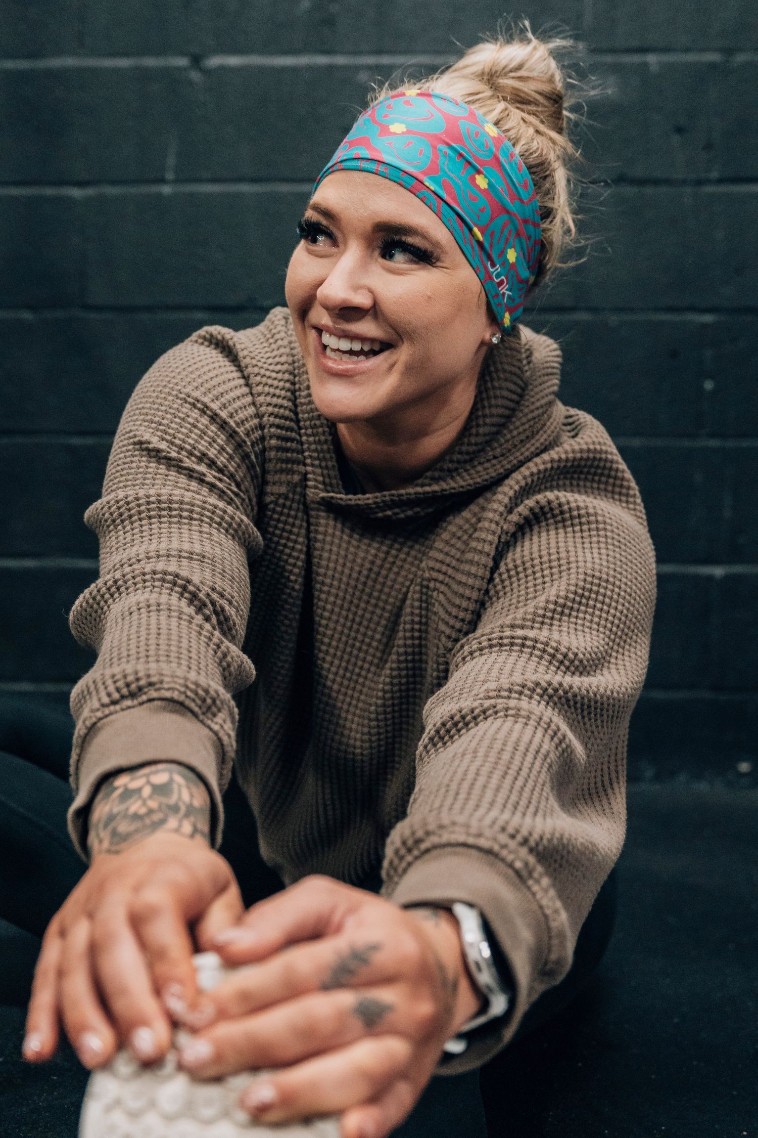 Athlete in brown sweater and patterned headband stretches against dark wall.