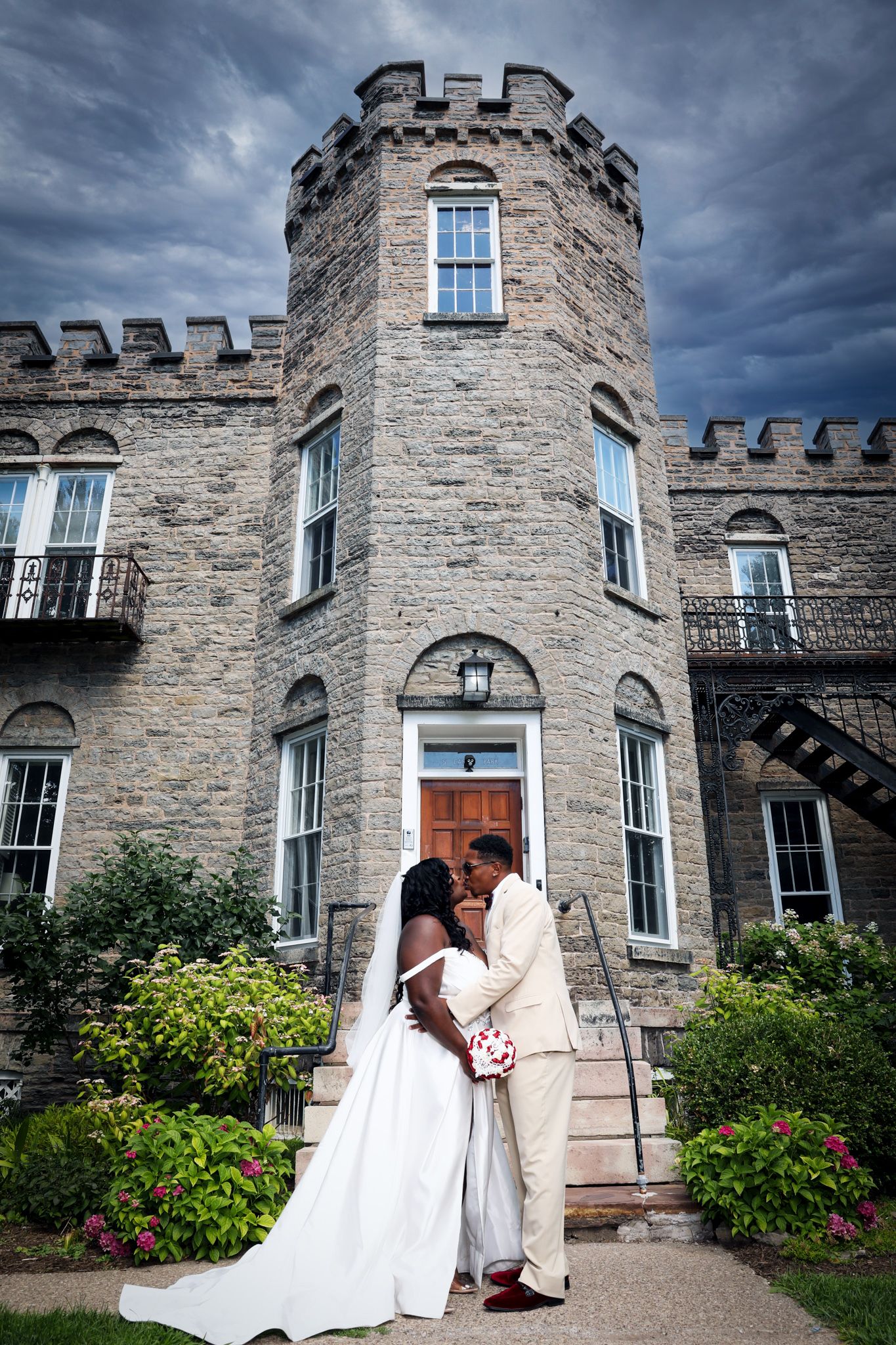 A wedding photoshoot in front of a grand stone castle with dramatic cloudy skies.