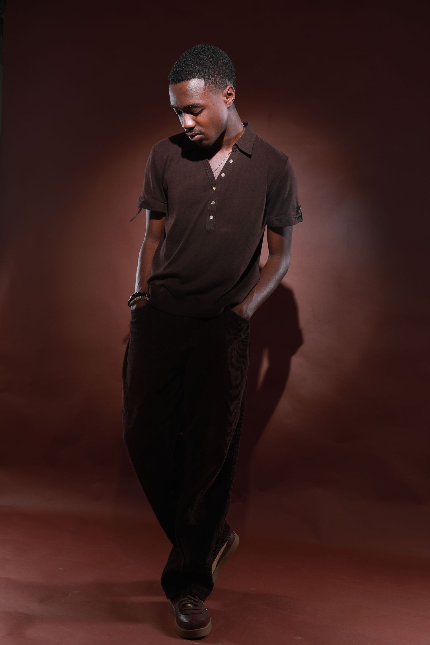 Moody portrait of person in brown polo shirt against dark burgundy backdrop.