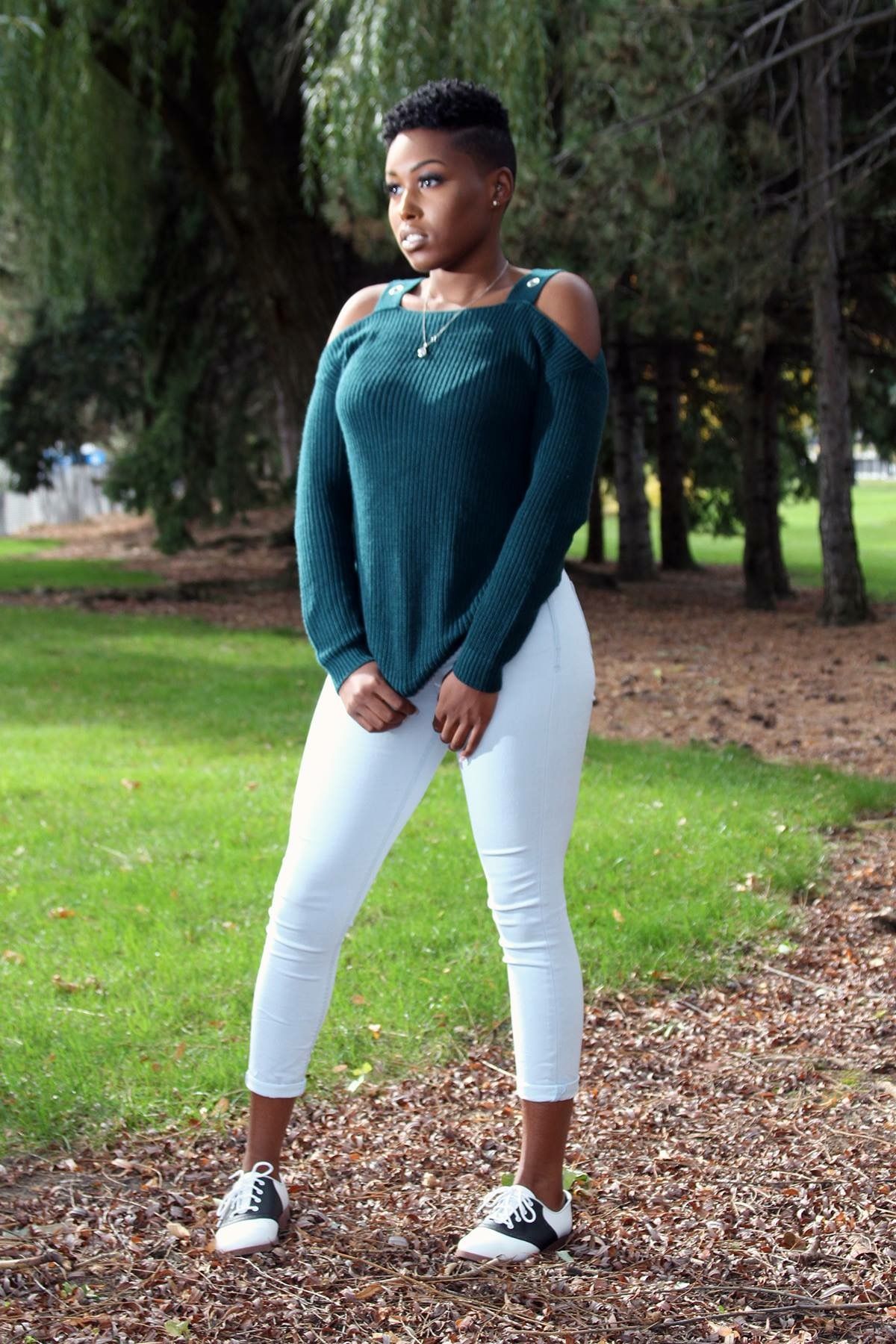 Outdoor portrait of person in teal sweater and white pants posed on woodland path.