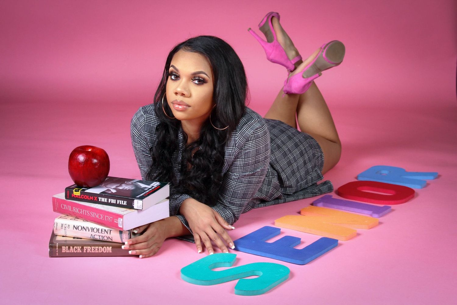 Artistic photo series of someone lying on pink background with books for senior portraits.