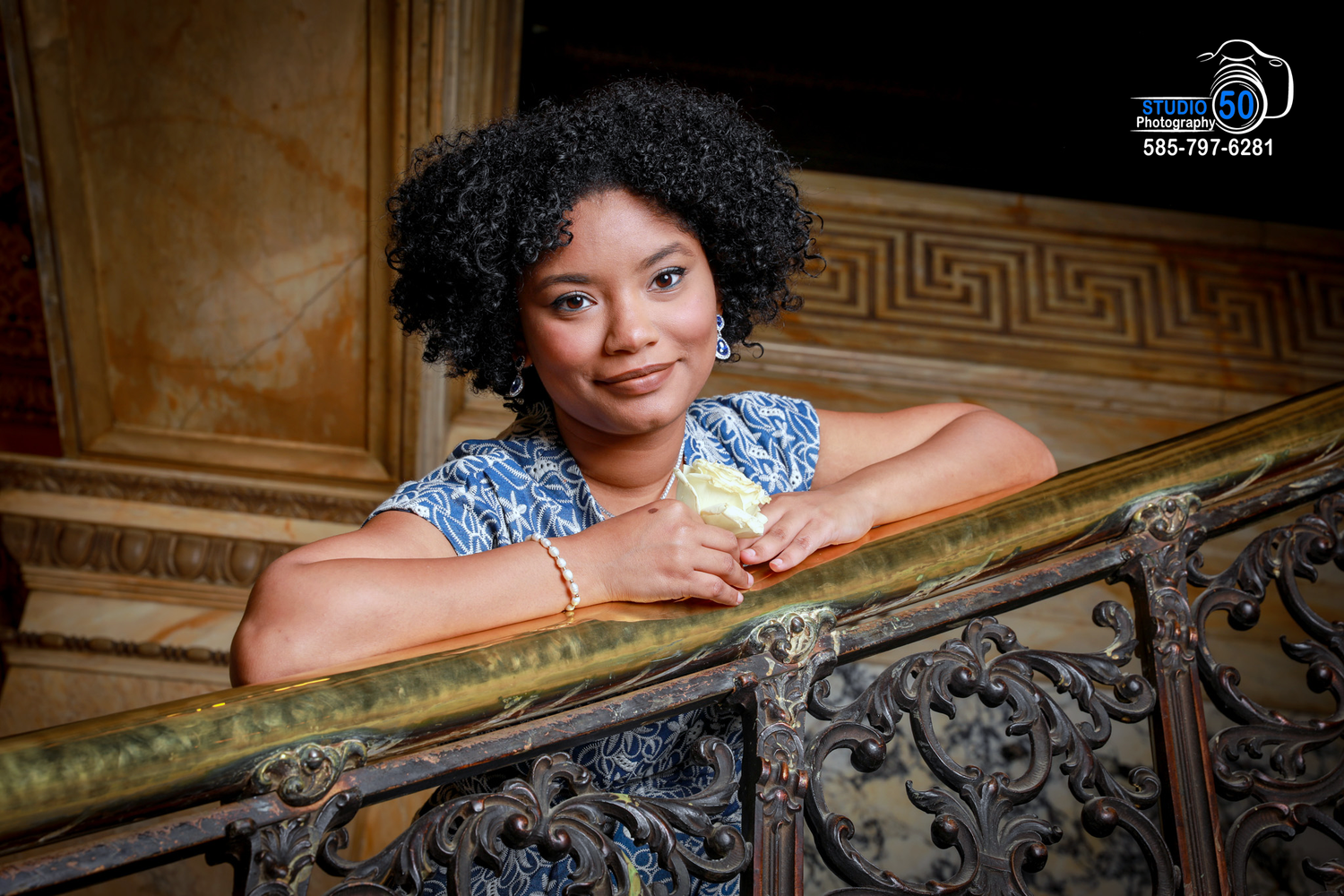 Person in blue floral dress poses by ornate wooden banister.