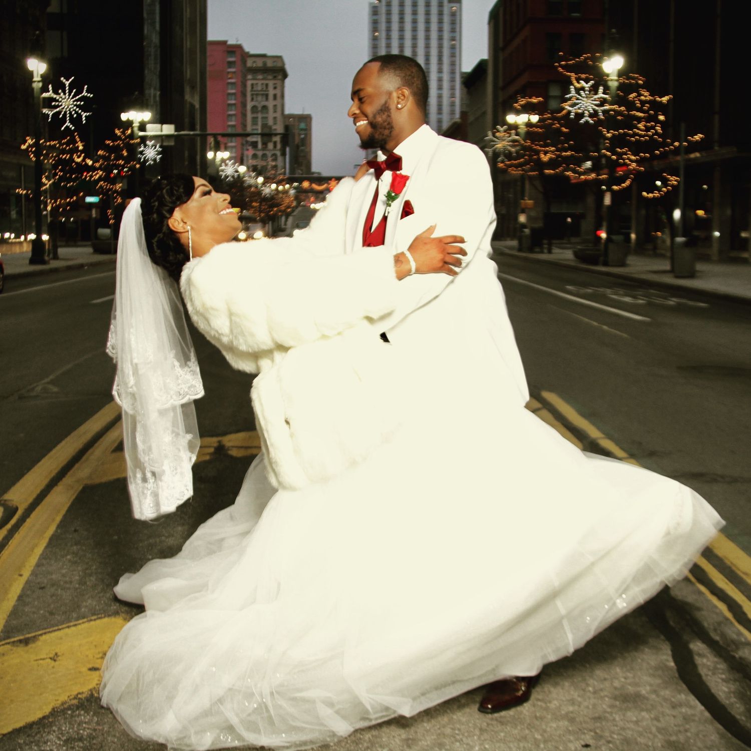 Romantic nighttime wedding photos on an urban street with city lights in background.