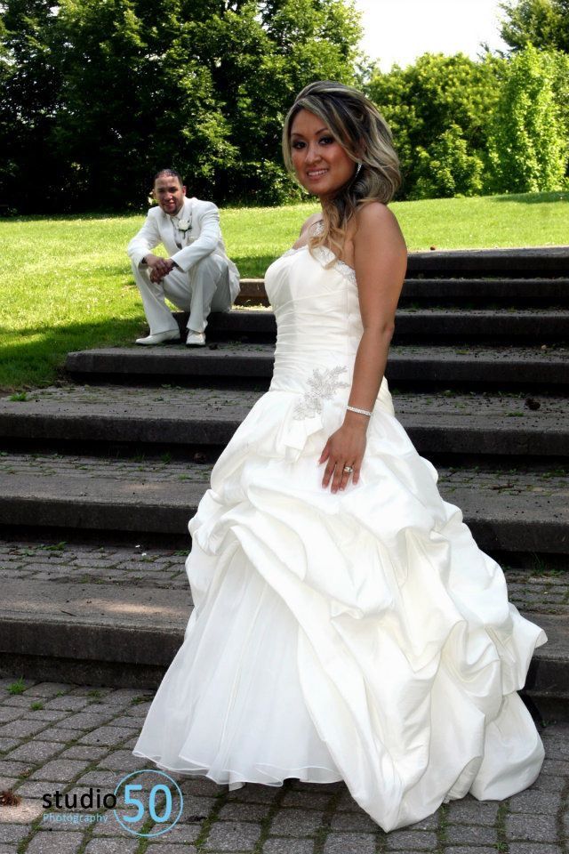Bride in flowing white dress posing on stone steps in a garden setting.
