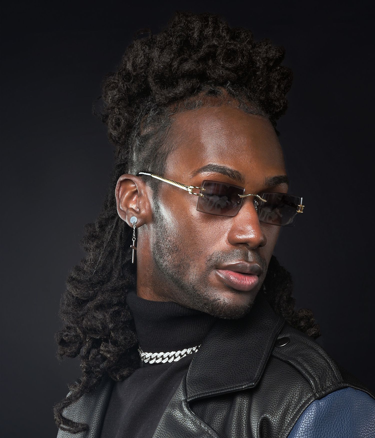 Dramatic studio portrait featuring leather jacket and silver chain necklace against dark background.
