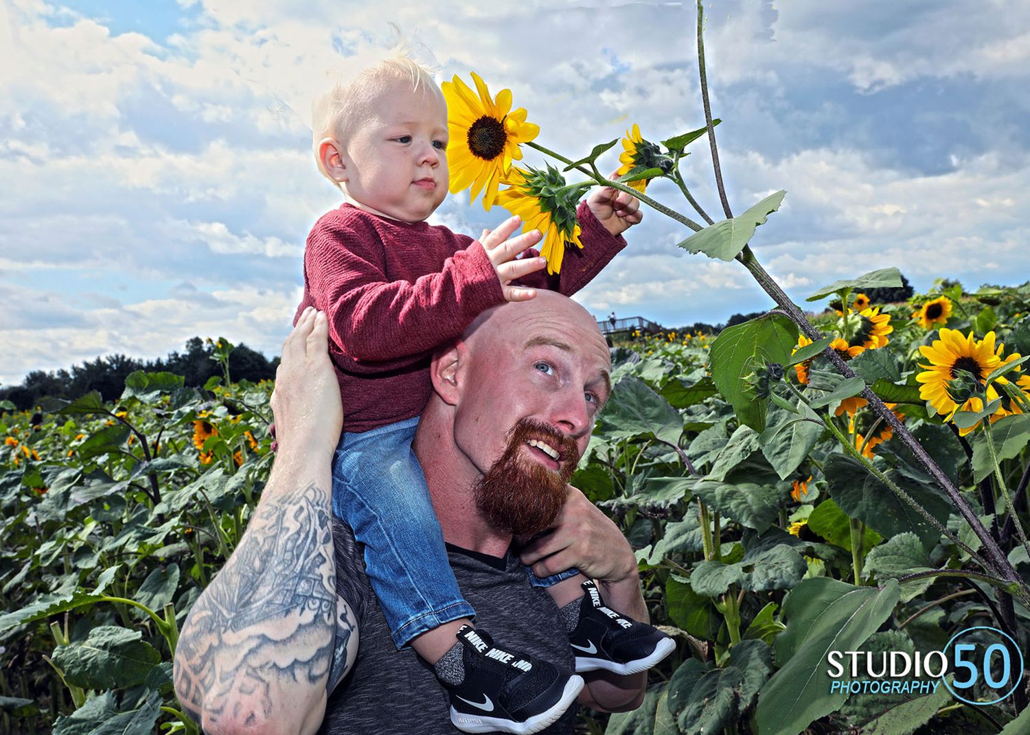 Father and child share joyful moments in blooming sunflower field on sunny day.
