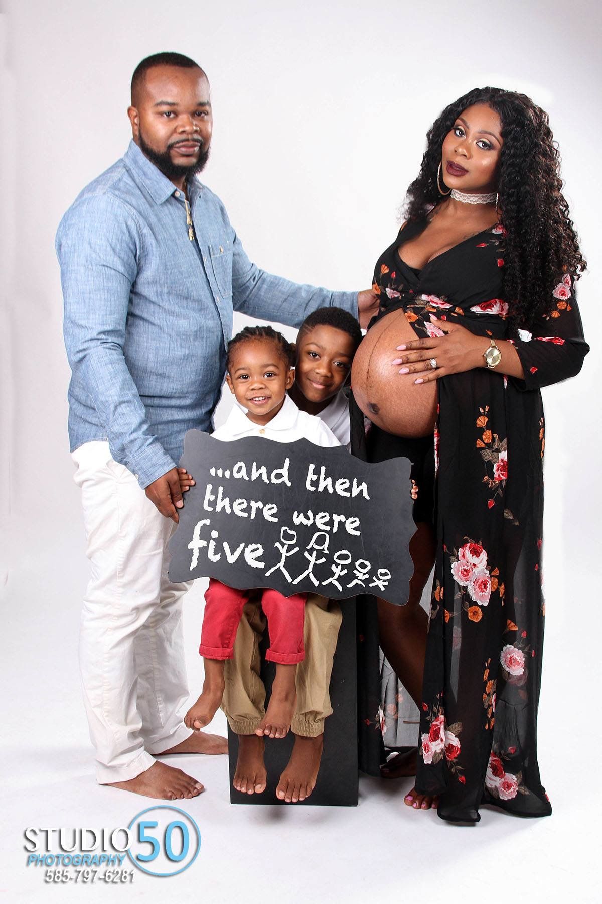 Studio family portrait with pregnancy announcement sign and floral dress.