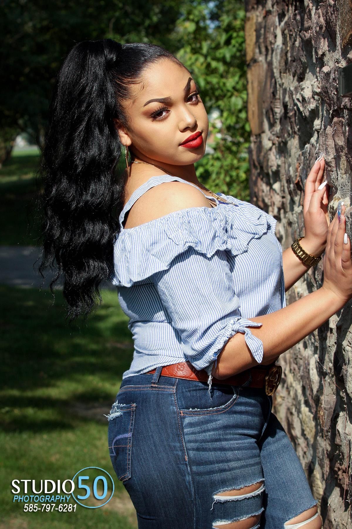 Outdoor portrait against tree wearing blue off-shoulder top and distressed jeans.
