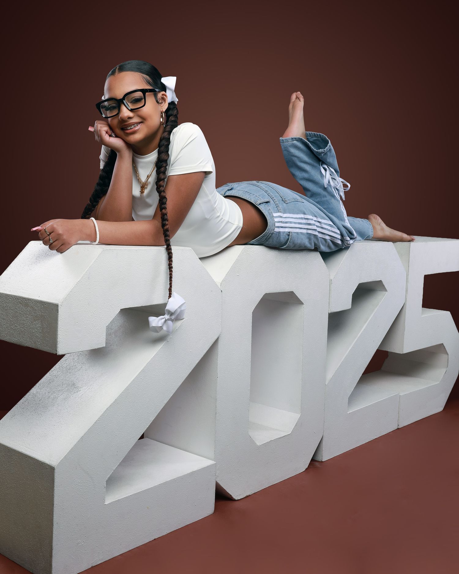 Senior portraits with large white 2025 numbers on brown studio backdrop.