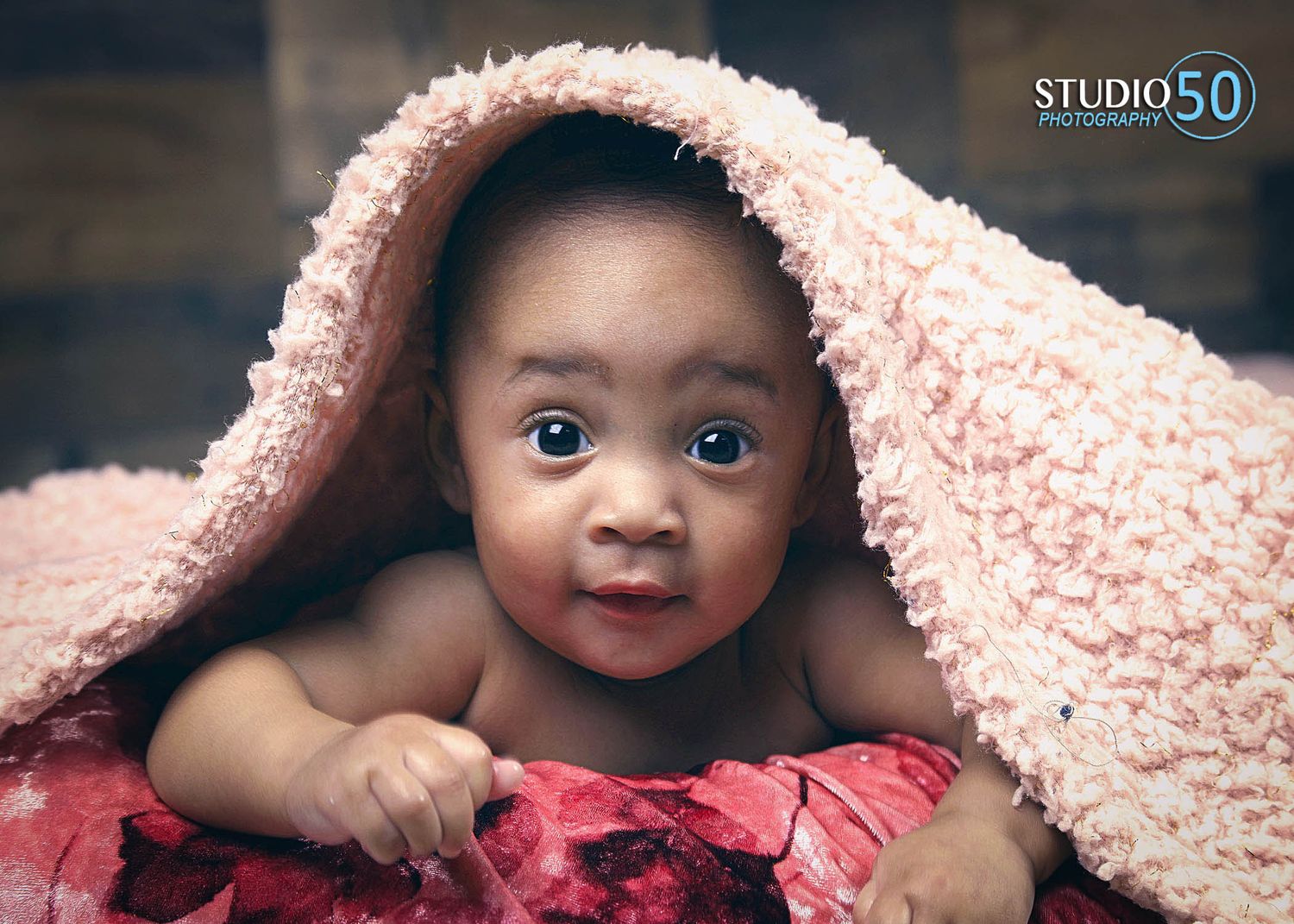 A baby in a soft pink blanket looking at camera with expressive eyes.