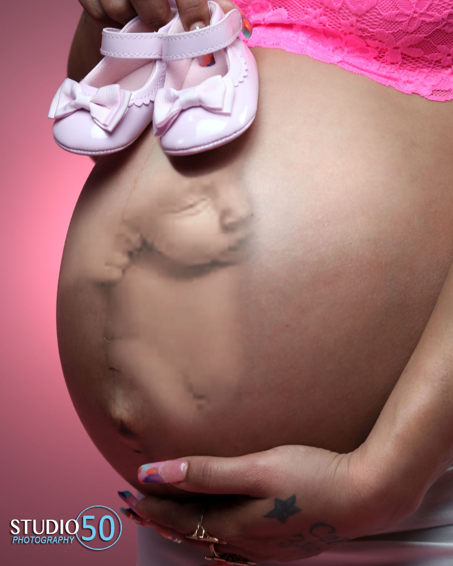 Pink-toned maternity photos focusing on pregnant belly with white bow details.