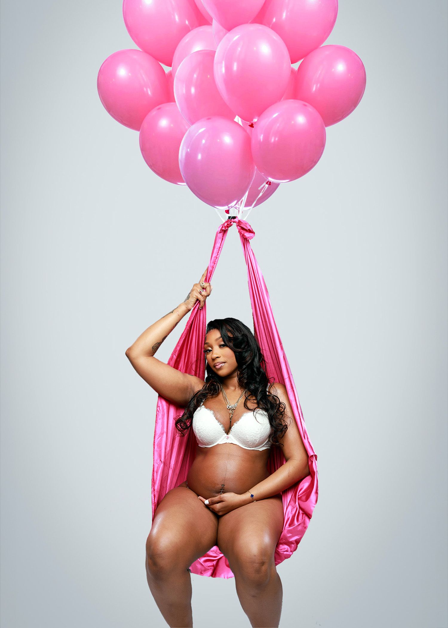 Maternity photo with pink balloons and fabric in dreamy studio setting.