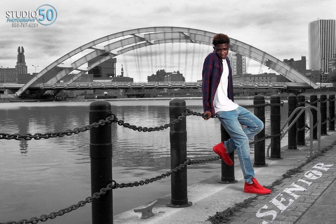 Person in casual wear poses on waterfront with arched bridge in black and white photo.