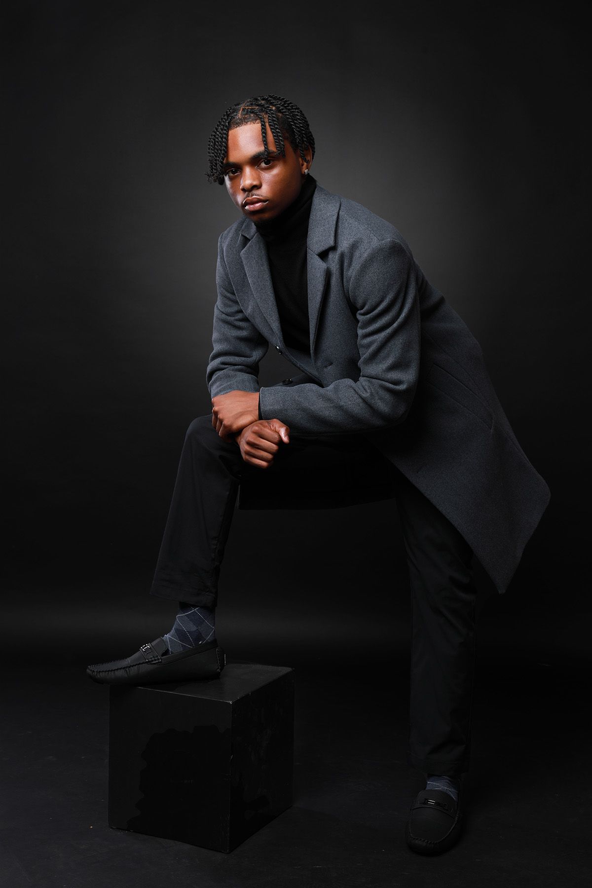 Moody fashion portrait in dark suit against black background with dramatic lighting.