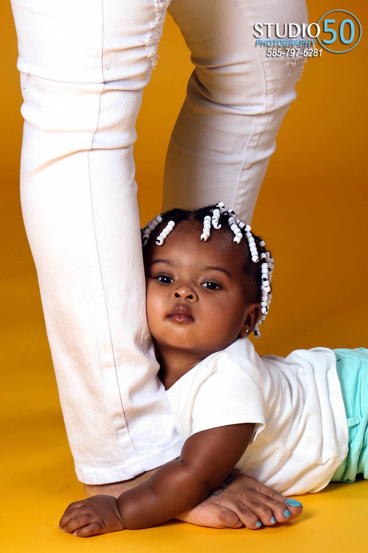 Creative baby portrait with white clothing against vibrant orange background at Studio 50.