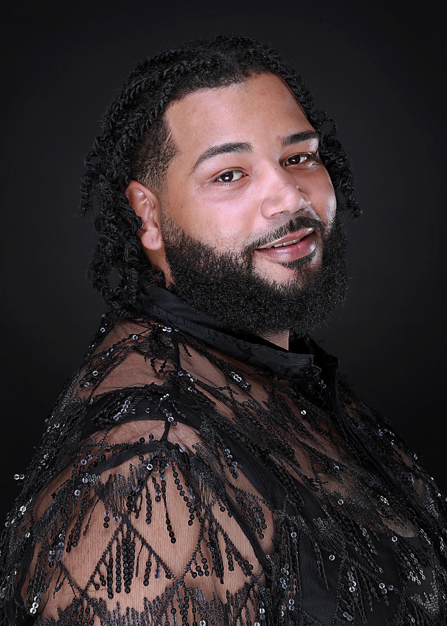 Portrait in sheer black lace outfit against dark studio background.