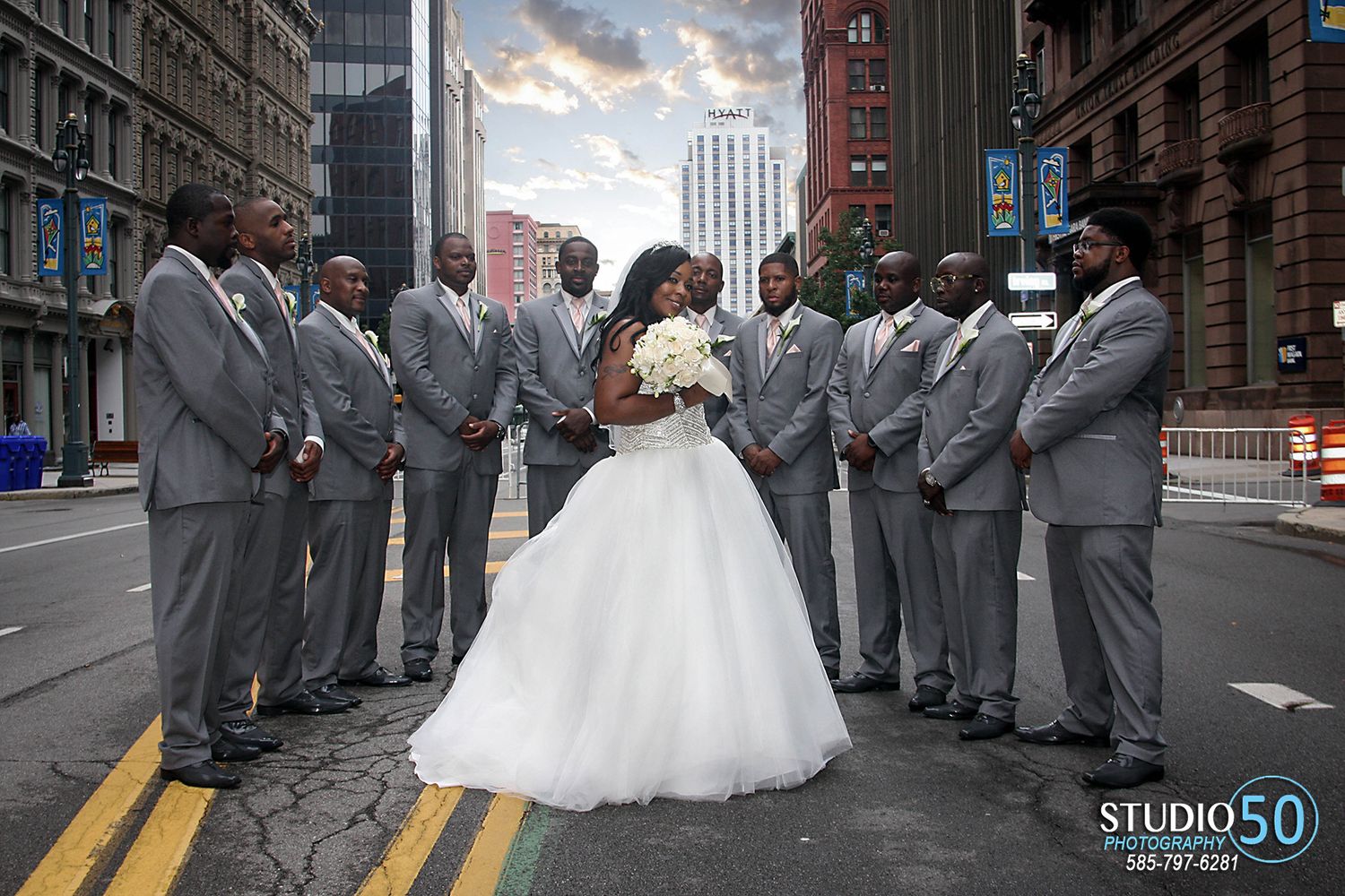 Wedding party in grey suits poses with bride in urban street setting.