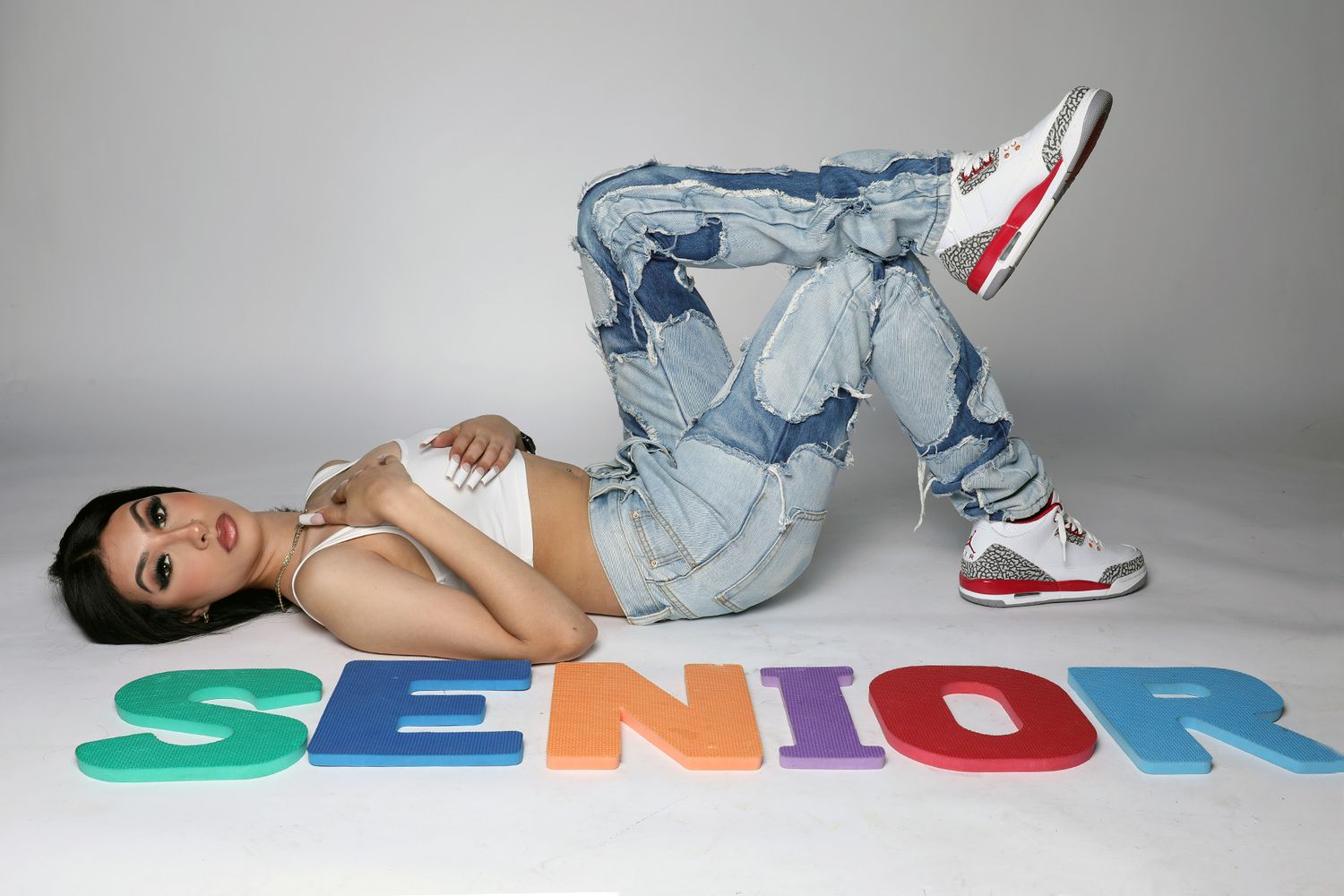 Student in denim lies beside colorful 'SENIOR' text for graduation photo.