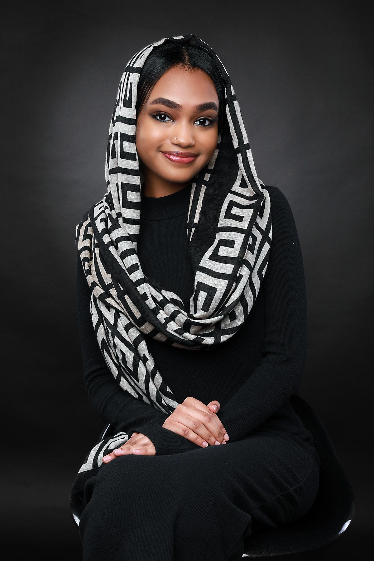 Professional studio portrait featuring a geometric black and white patterned scarf and black turtleneck against dark background.