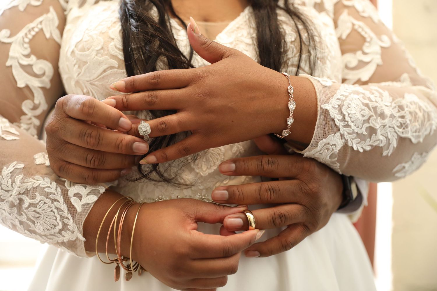 Close-up of hands showing engagement or wedding rings against a lace background.