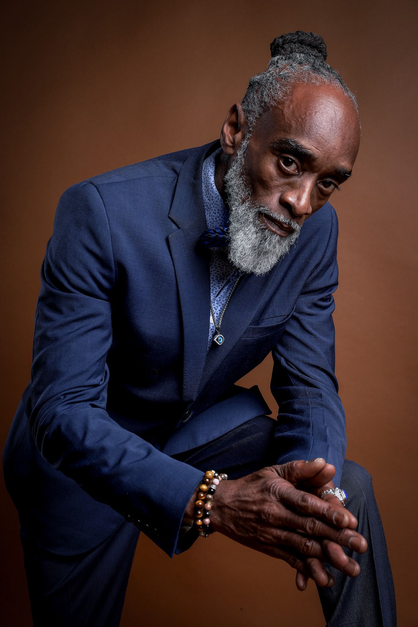 Artistic portrait series showing a distinguished man in navy suit against brown backdrop in varying contemplative poses.