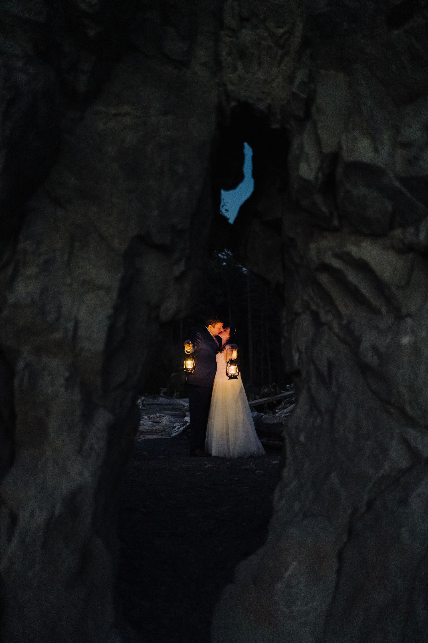 A ethereal wedding photo in a dark cave illuminated by glowing lanterns with a peek of blue sky above.