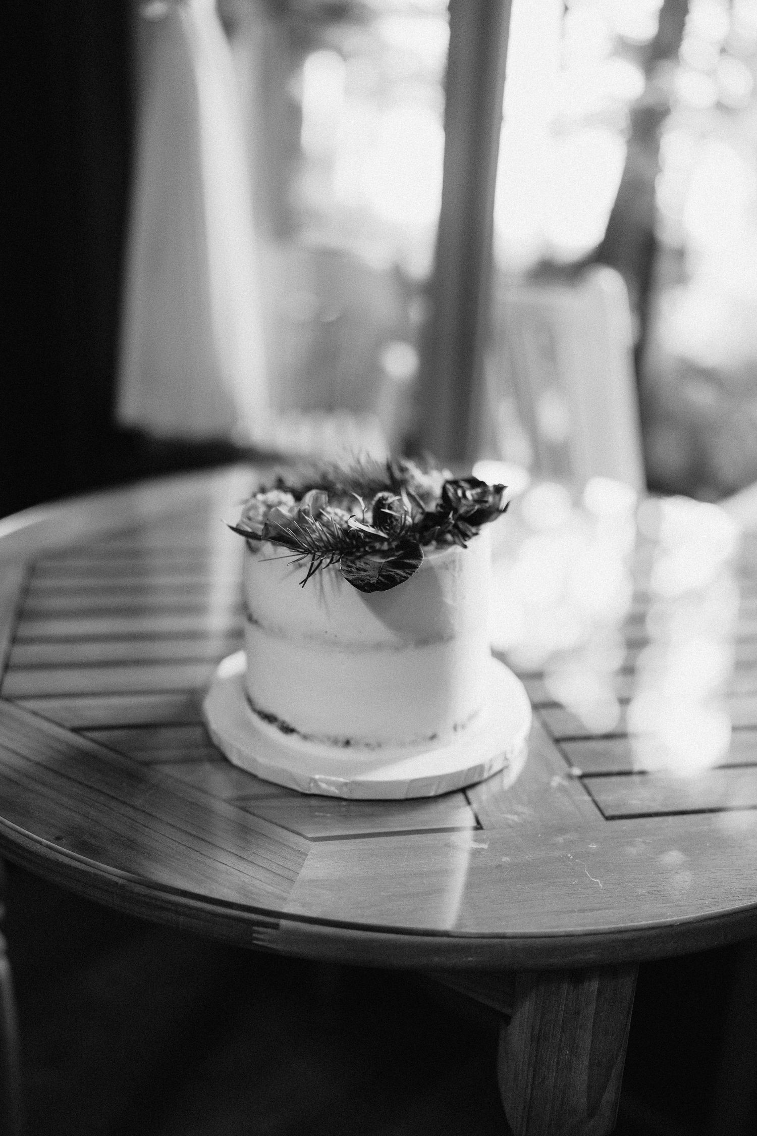 A minimalist white wedding cake with dried flower decorations on a wooden table.