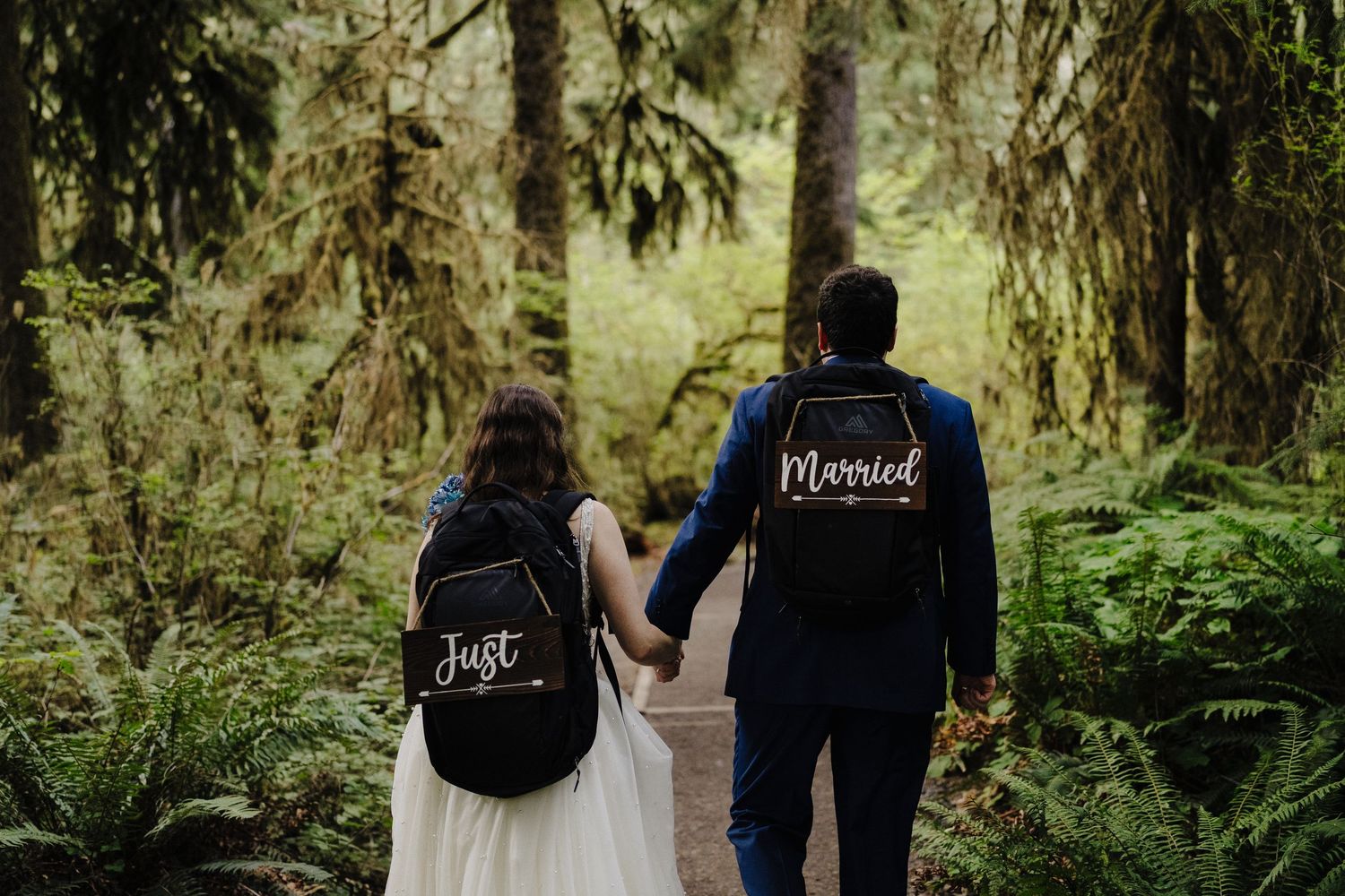 A couple wearing 'blessed' jackets holds hands while walking through a lush forest.