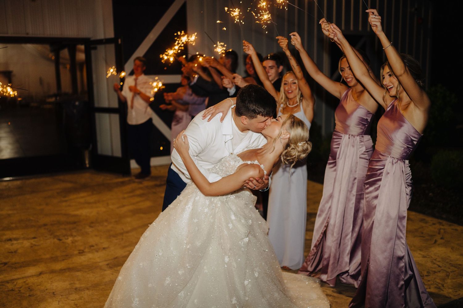 Wedding party dancing and celebrating with raised arms on a wooden dance floor.