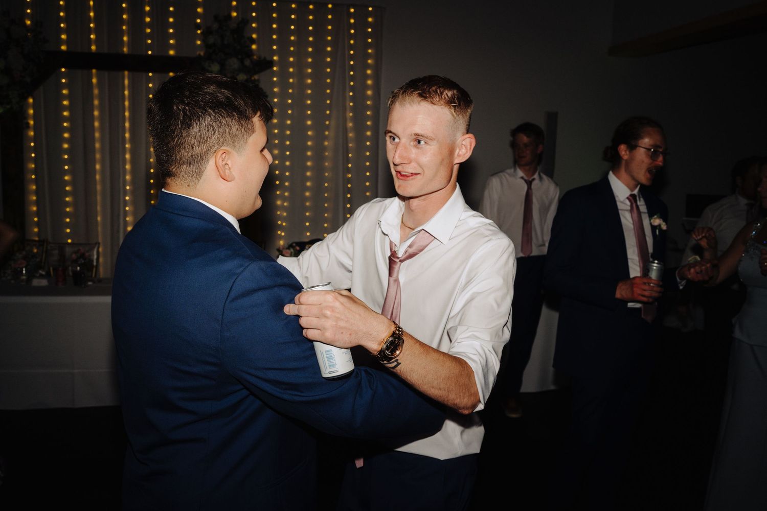 Two guests slow dancing at wedding reception with string lights in background.
