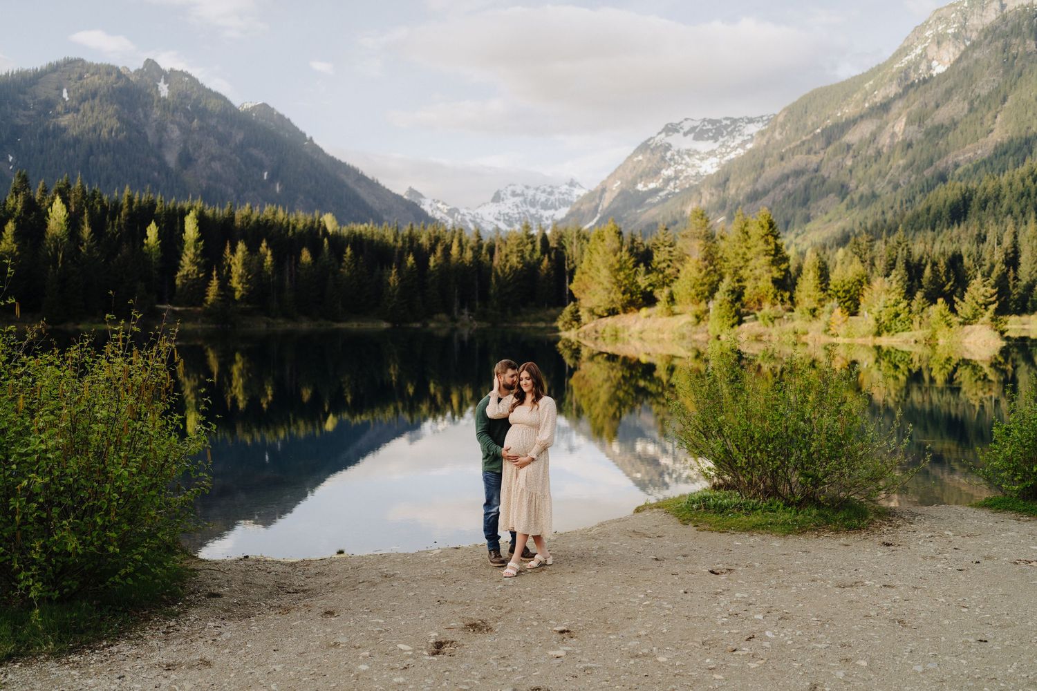 Scenic mountain lake surrounded by evergreen forest and snow-capped peaks reflecting in calm waters at sunset.