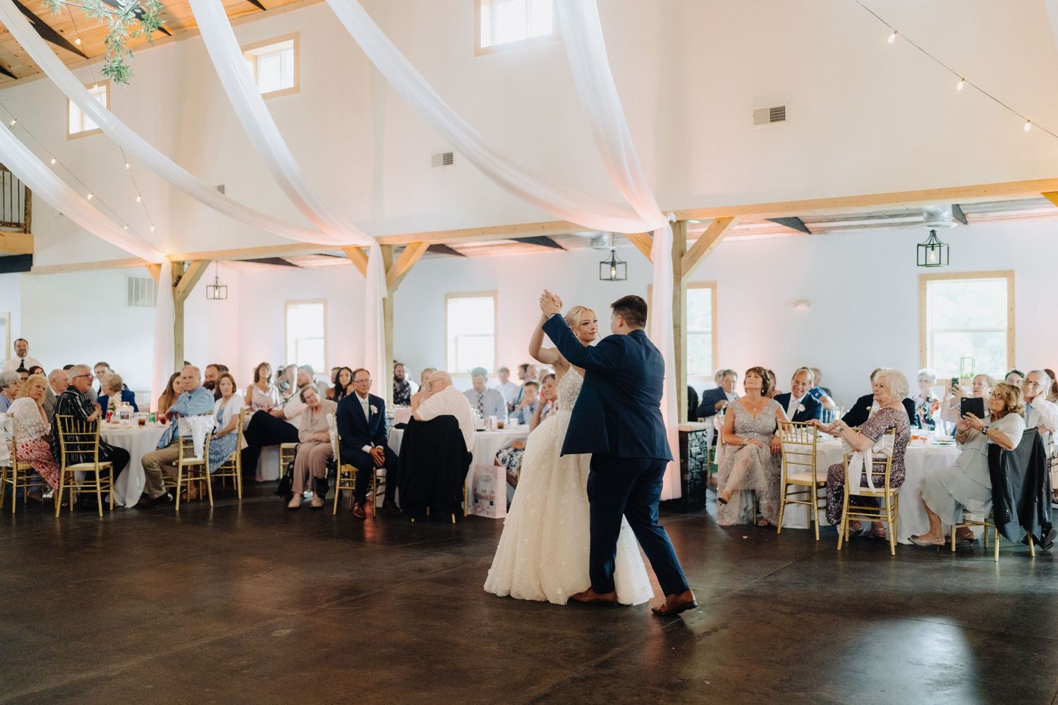 Panoramic view of an elegant white wedding reception hall with draped fabric and table settings.