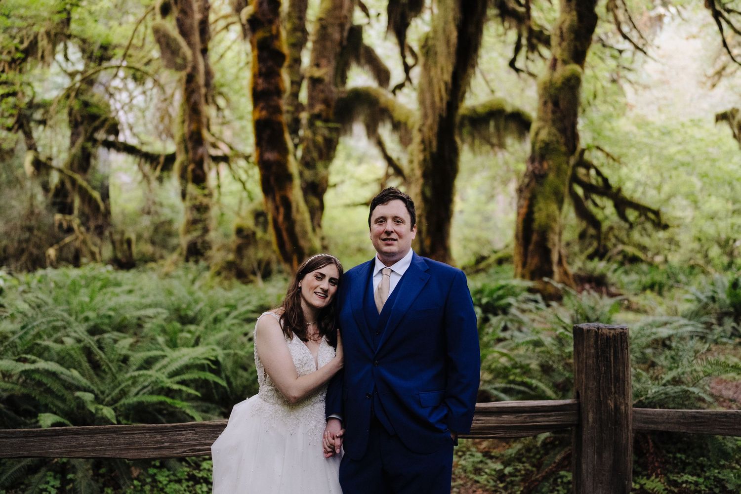 Wedding couple poses together in lush green Pacific Northwest forest.