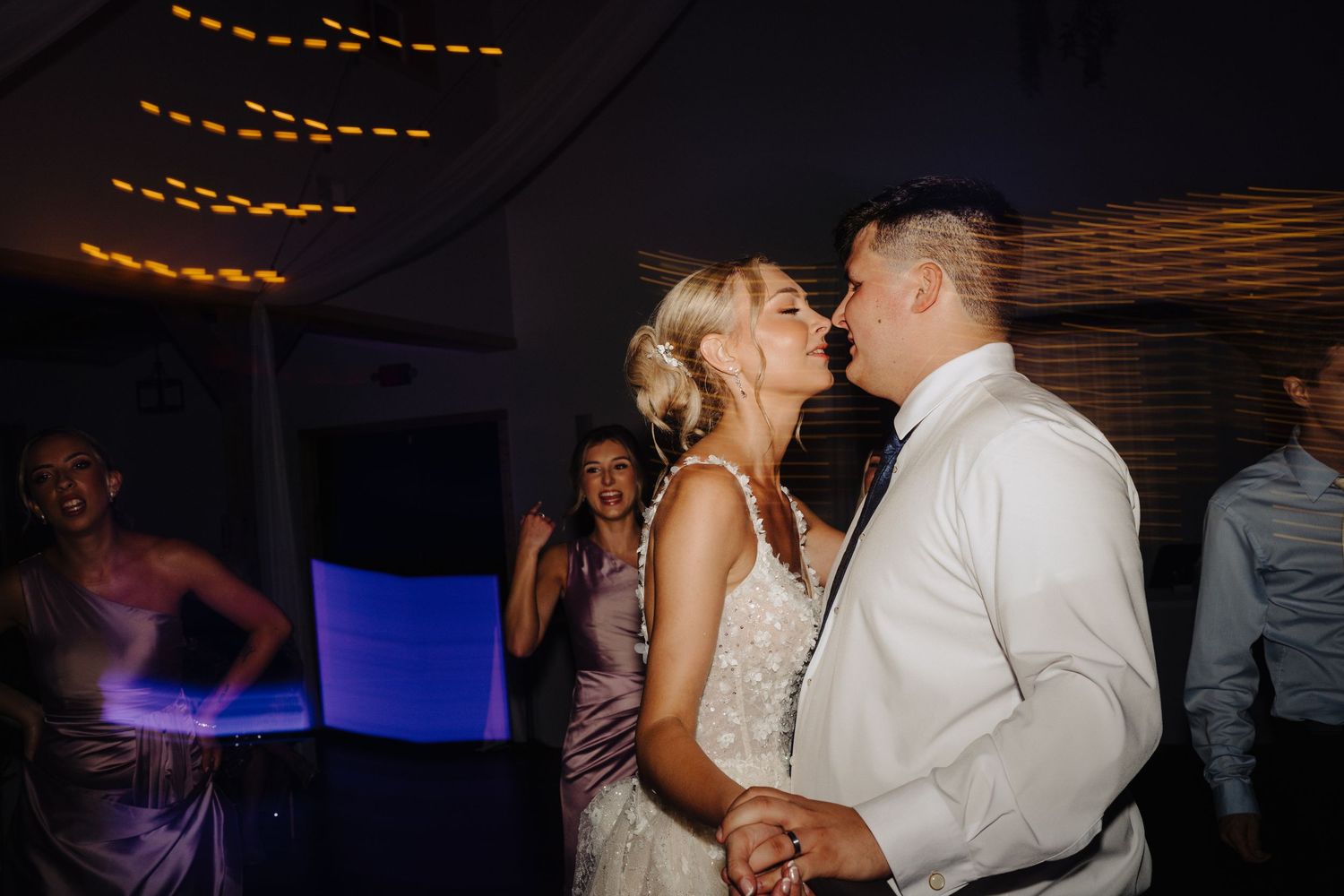 Couple sharing intimate dance moment under amber string lights at reception.