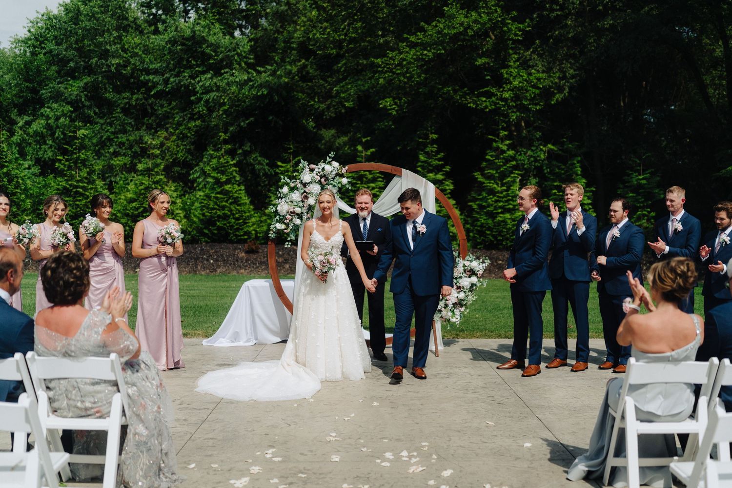Wedding ceremony setup in a garden with white chairs and floral decorations.