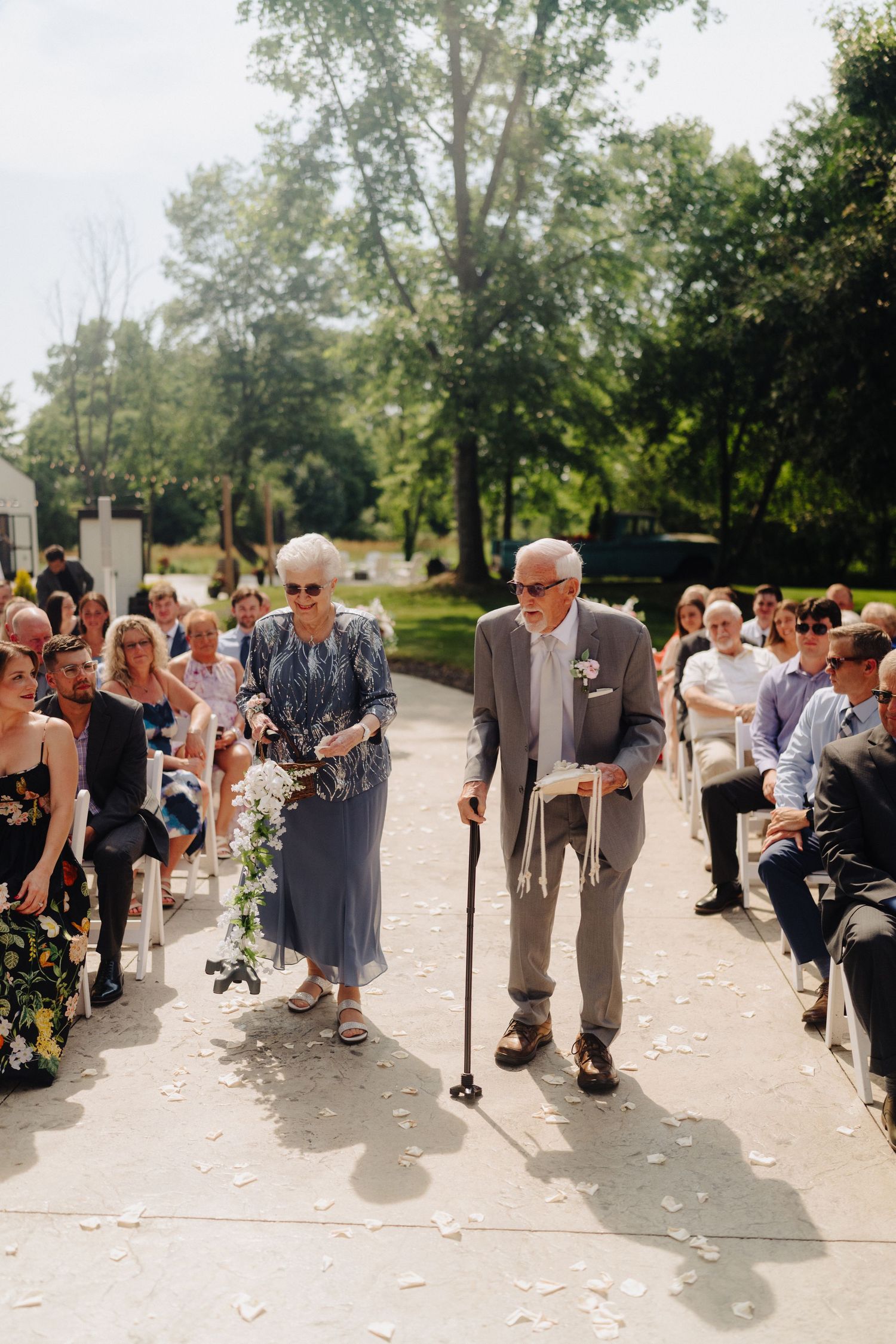Wedding ceremony guests lined up along a paved outdoor pathway on a sunny day.