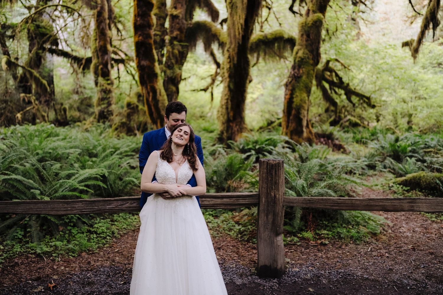 Wedding moment captured in a lush green mossy forest with wooden railing.