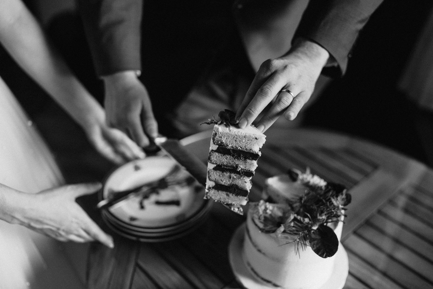 Black and white photo showing hands cutting into layers of a wedding cake.