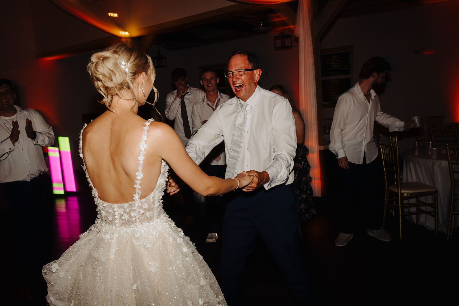Wedding reception guests dancing in a dimly lit venue with red ambient lighting.