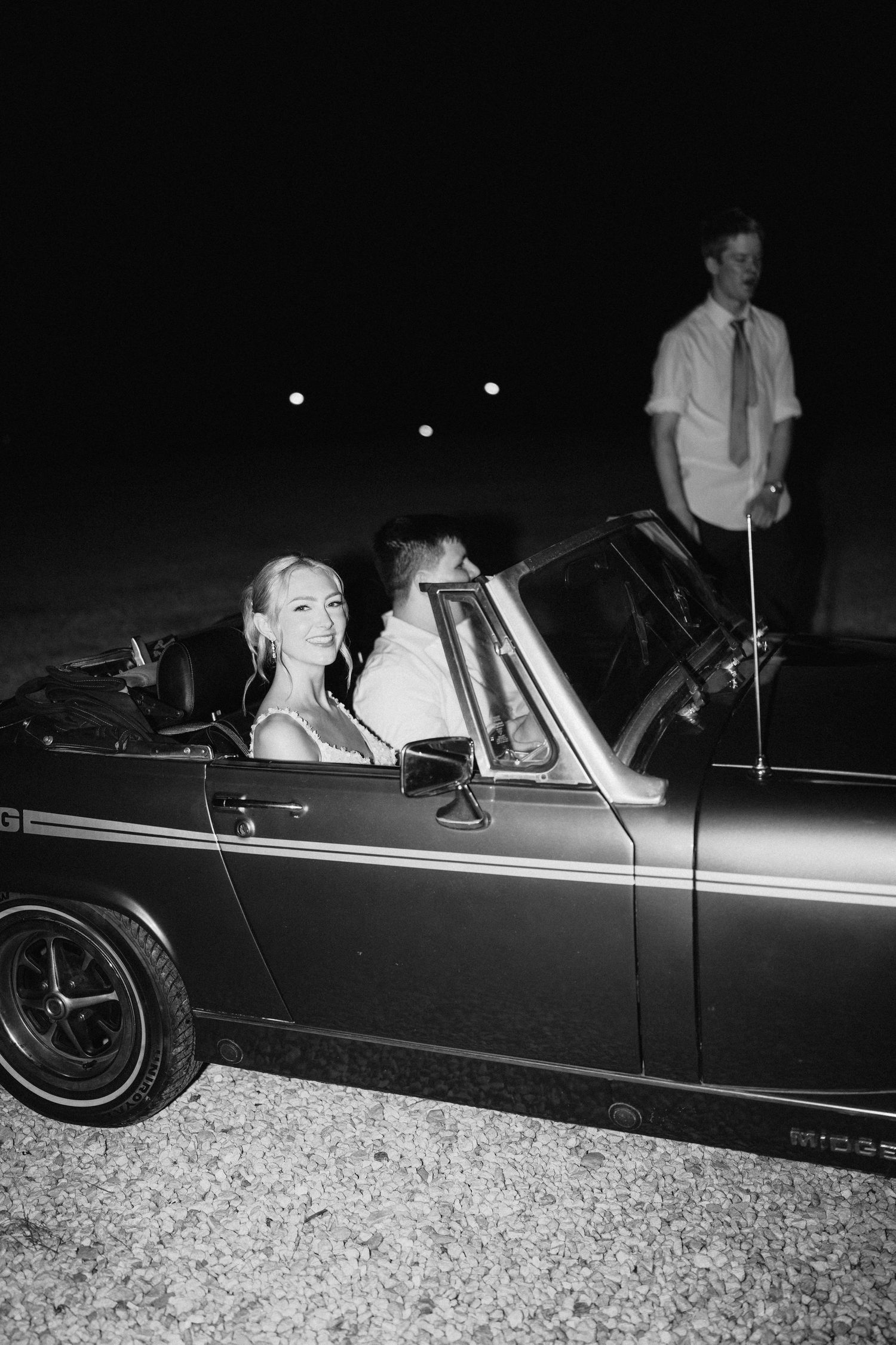 A classic convertible car illuminated by flash photography during a nighttime wedding exit.