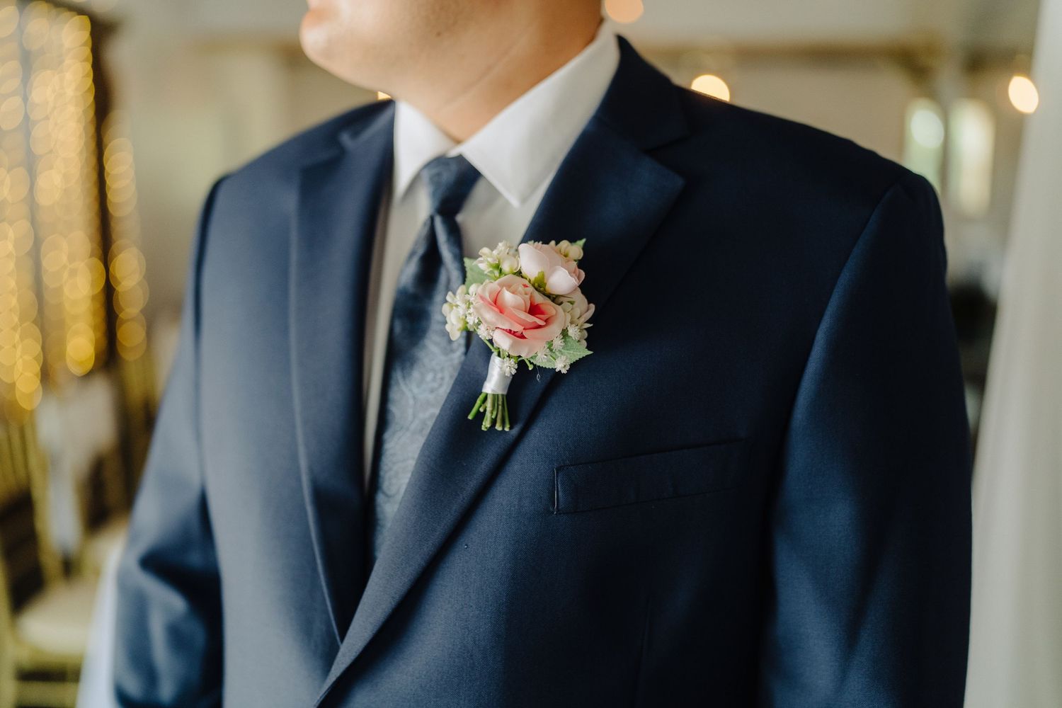 A couple shares a joyful moment during their wedding reception with the groom wearing a navy suit and pink boutonniere.