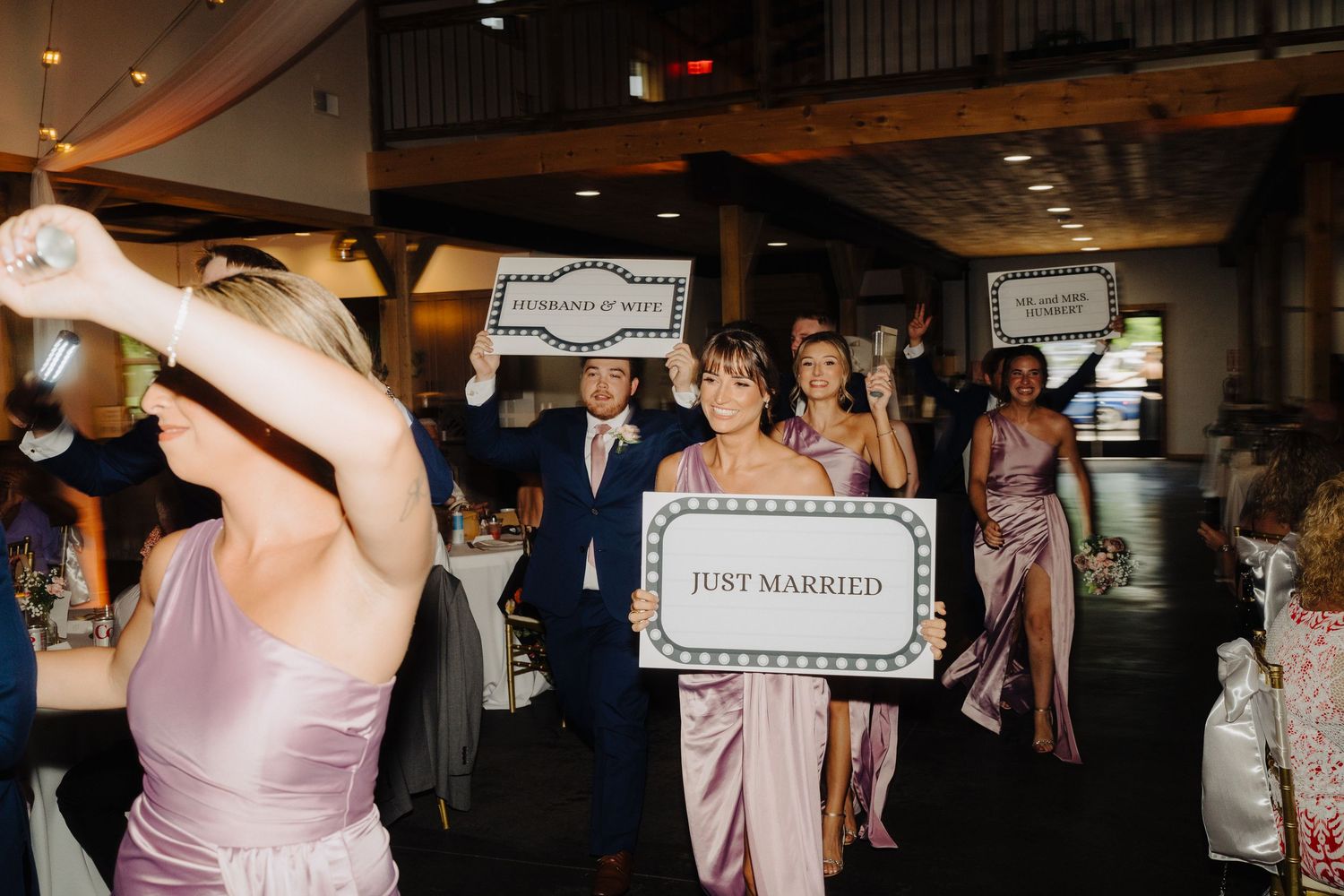 Wedding reception celebration with guests holding 'Just Married' sign in rustic venue.