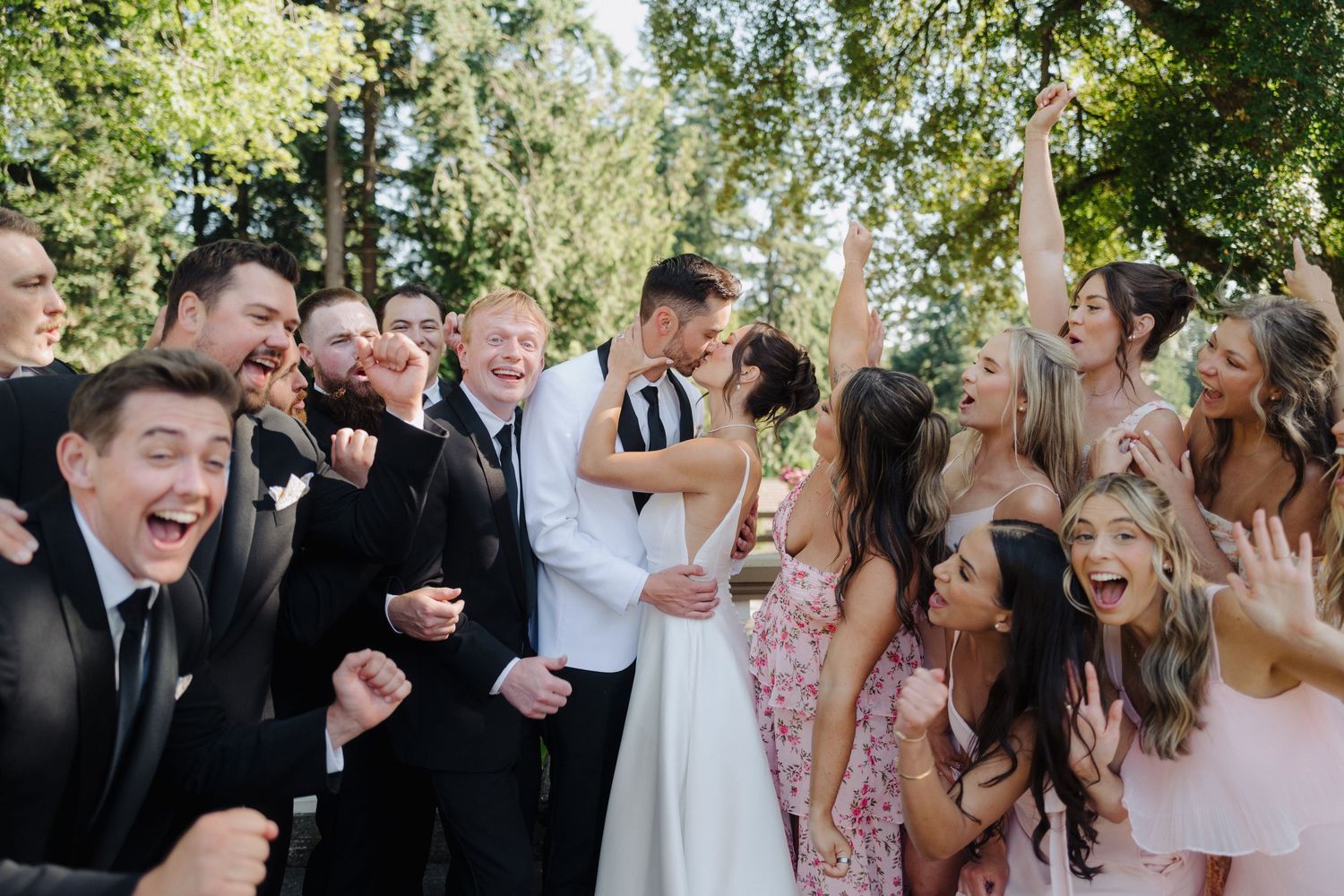 Wedding party members laugh and celebrate together during an outdoor photo session in natural lighting.