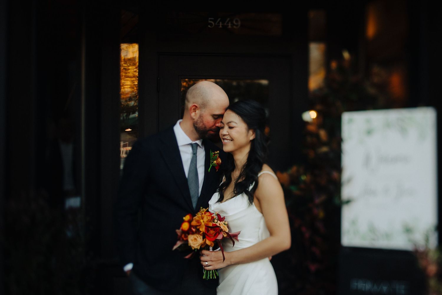 A romantic moment captured at dusk as a couple in wedding attire embrace while holding an autumn-colored bouquet.