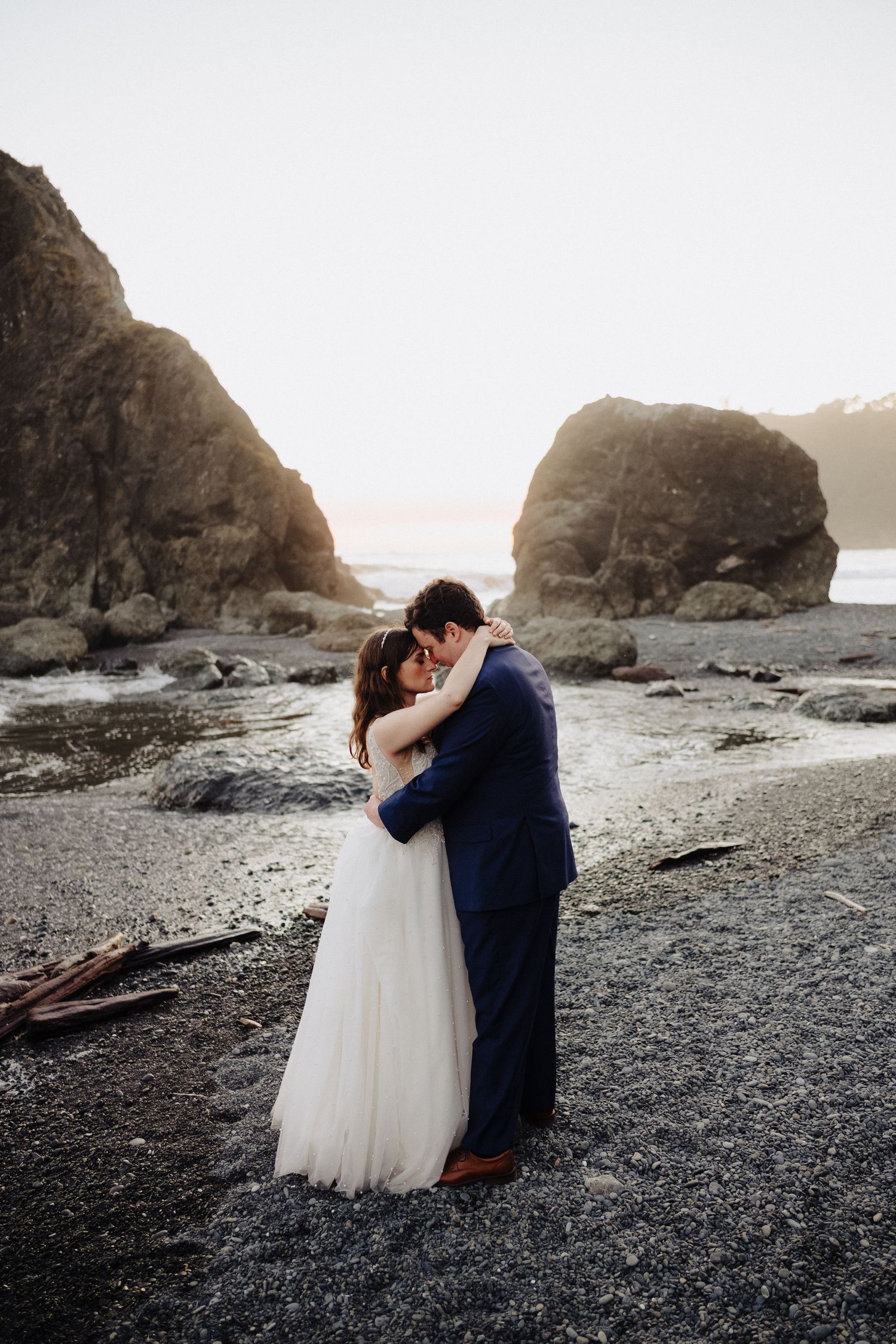 Intimate wedding moment captured between rocky coastal formations at golden hour.