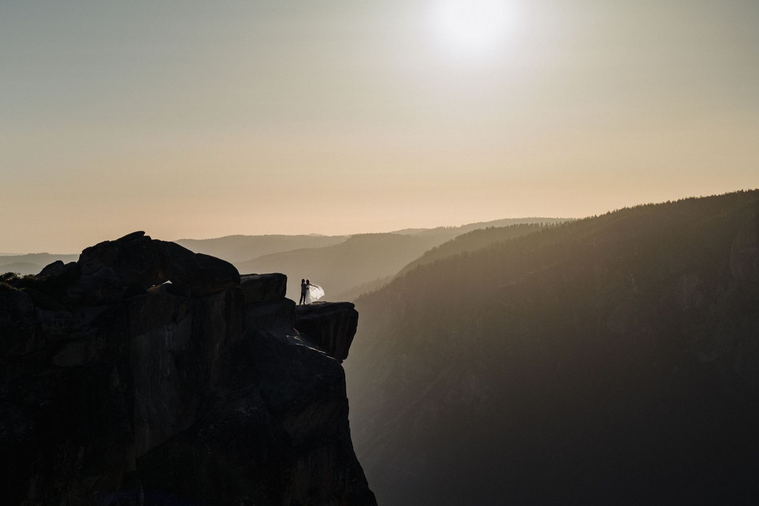 Silhouette of wedding on a cliff edge against dramatic sunset sky.