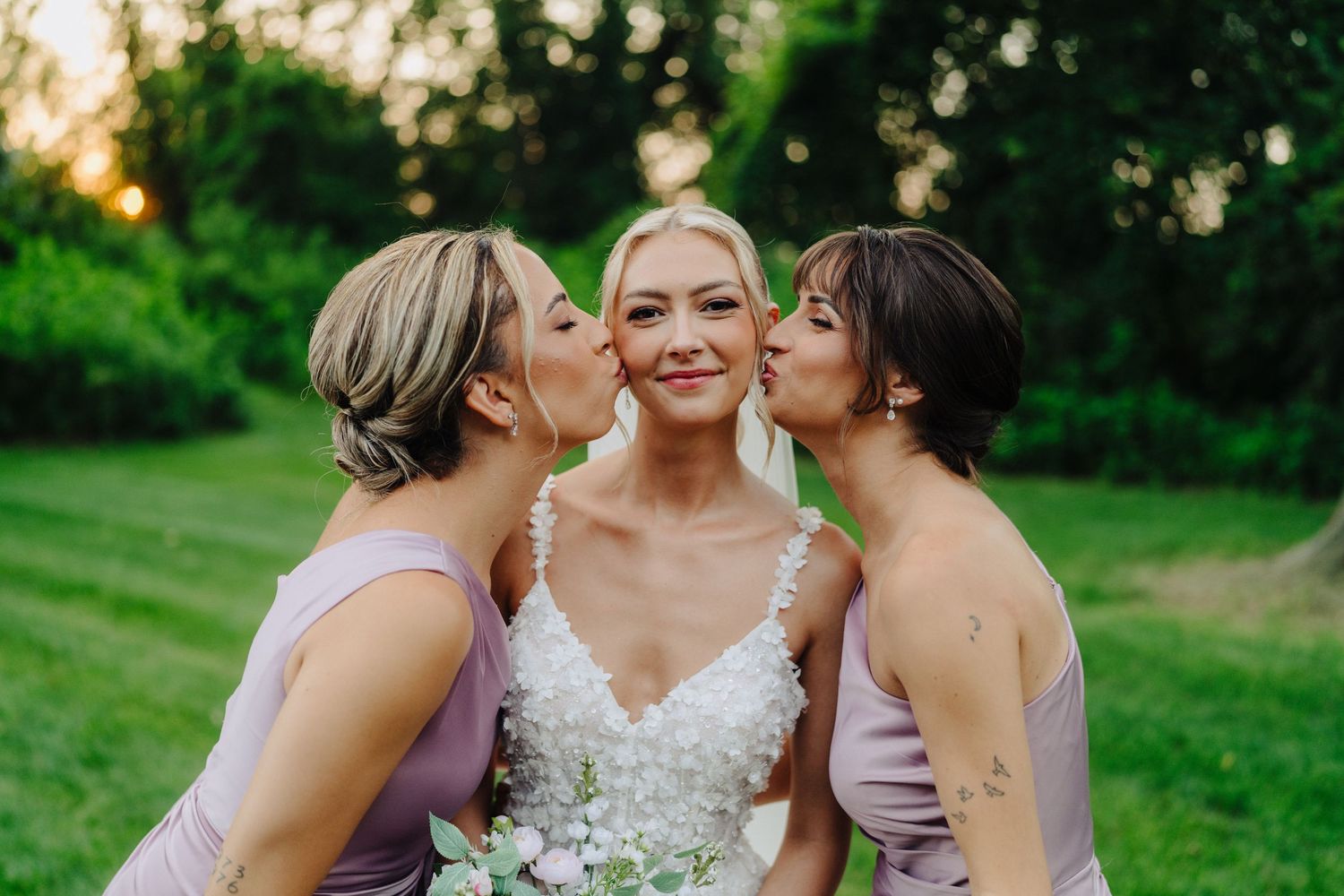 Bridesmaids in lavender dresses share a joyful moment with the bride in a lush outdoor garden setting.