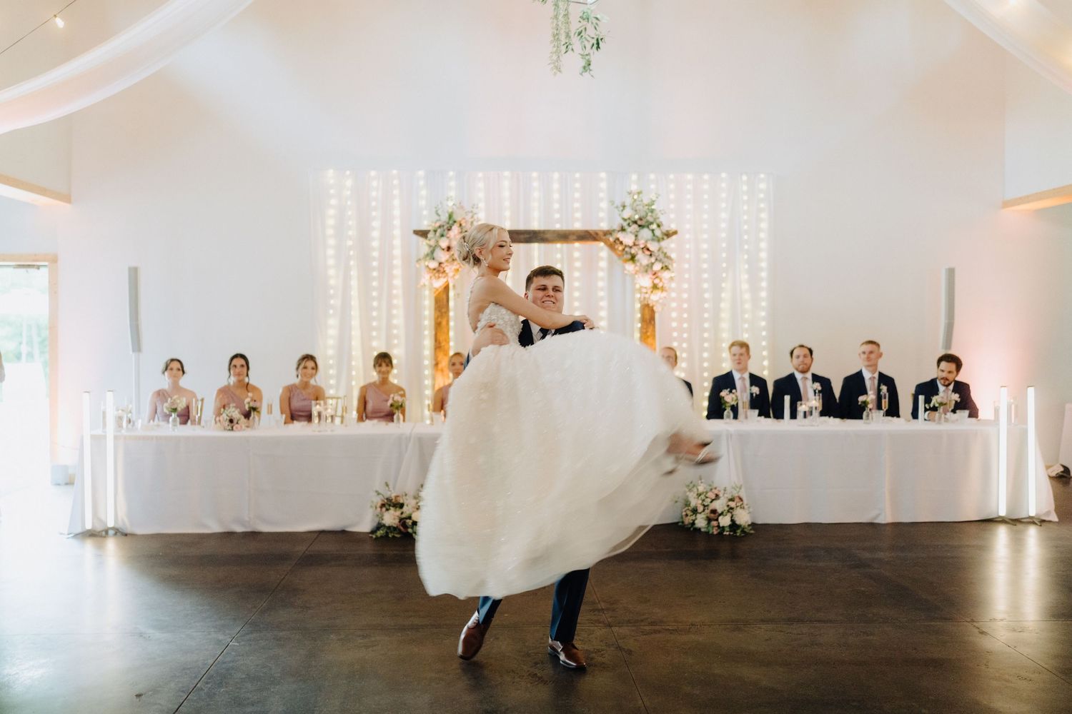 Wide angle view of a minimalist white wedding venue with hanging lights and floral arrangements.