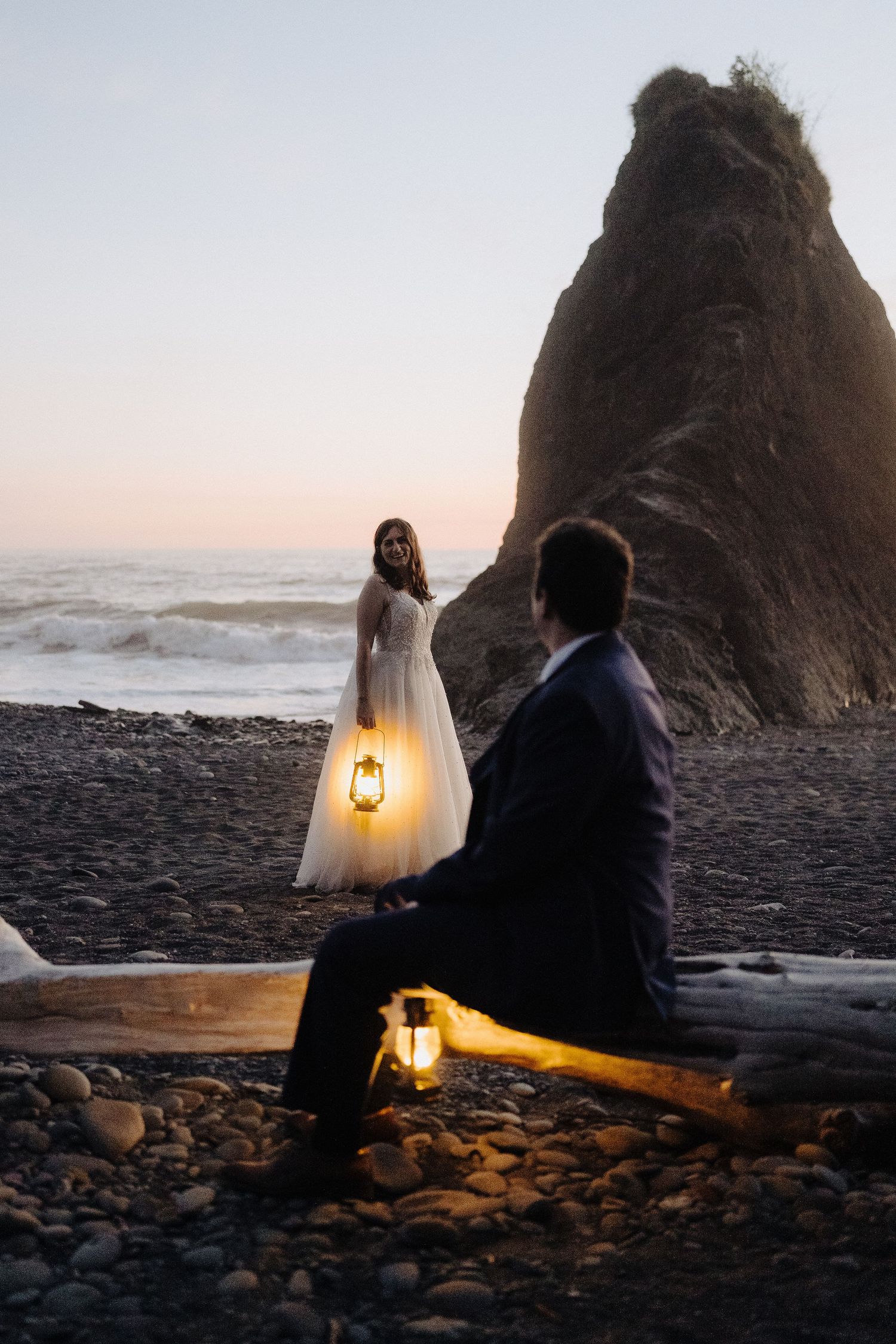 A romantic beach scene with lantern light and dramatic rock formation at dusk.
