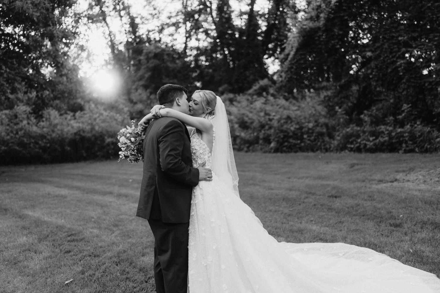 Black and white portrait of newlyweds embracing outdoors during sunset.